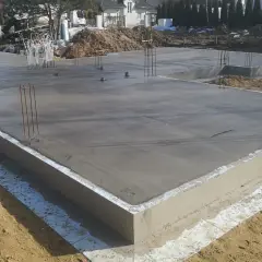 Świeżo wylany betonowy fundament pod dom, z wystającymi prętami zbrojeniowymi. To kluczowy etap, jak zrobić fundament pod dom, zapewniający stabilność konstrukcji.