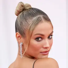 Elegancka, gładka fryzura typu sleek bun z błyszczącymi kolczykami.