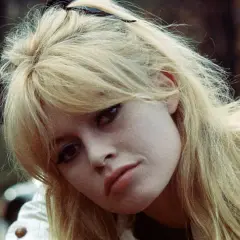 Blonde Frau mit langen Curtain Bangs, die leicht zerzaust sind. Ihr Blick ist nach unten gerichtet.
