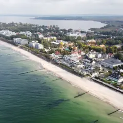Widok z lotu ptaka na nadmorską miejscowość Mielno, z plażą, morzem i zabudowaniami. Ile mieszkańców ma Mielno? Tego nie widać, ale jest tu pięknie.