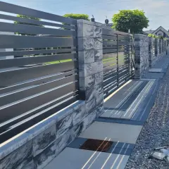 Nowoczesne ogrodzenie przed domem z szarego metalu i kamiennych bloczków, z bramą wjazdową i furtką.