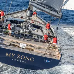 Equipaggio in rosso sul My Song yacht, che solca le onde blu. La vela nera e bianca cattura il vento.