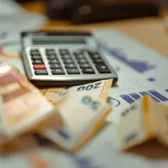 Kalkulator, banknoty euro i wykresy na biurku.