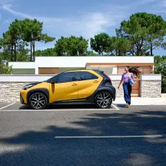 Une jeune femme se dirige vers sa voiture jaune et noire, une **voiture jeune permis automatique** parfaite pour débuter.