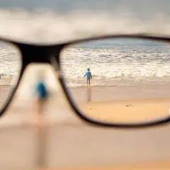 Okulary korygujące widok na plażę z dziećmi wchodzącymi do morza.