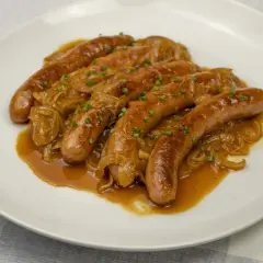 Salchichas doradas en salsa de cebolla caramelizada, un plato delicioso para aprender como hacer salchichas caseras.