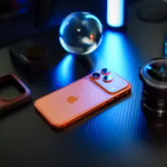 Pomarańczowy iPhone, skórzane etui i obiektyw na czarnym blacie. Idealna konfiguracja iPhone dla fotografa.
