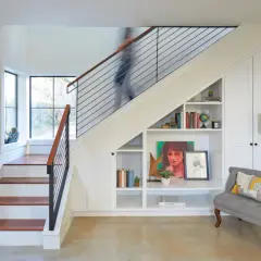 A person ascends a modern staircase, its sleek design contrasting with the built-in bookshelves and storage beneath. This stairwell is a functional art piece.