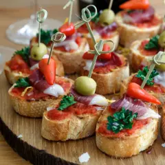 Pyszne przekąski sałatki na imprezę: kanapeczki z pomidorami, oliwkami, papryczkami i wędliną na drewnianej desce.