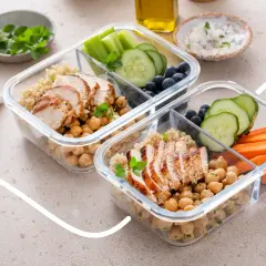 Zwei Behälter für Meal Prep mit Hähnchenbrust, Kichererbsen, Quinoa, Gurke, Karotten und Blaubeeren.