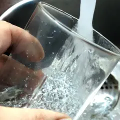 En hand håller ett glas som fylls med vatten från en kran. Ja, kan man drikke vann fra springen i Sverige, det är rent och gott!