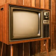 Stary telewizor z drewnianą obudową i ekranem, jak pierwszy telewizor, stoi na tle drewnianej ściany.