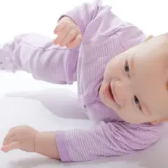 Uśmiechnięty niemowlak w fioletowym pajacyku uczy się obracać. To świetna zabawa i ważny etap rozwoju.