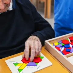 Un senior concentré assemble un puzzle coloré, un jeu mémoire senior stimulant.