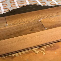 Close-up of plank flooring installation over underfloor heating. Wooden planks are being laid with spacers, showing the adhesive and heating elements beneath.