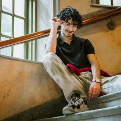 Malte Gårdinger sitter på en trappa med en röd tröja runt midjan.
