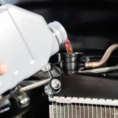 Ręka wylewa różowy płyn chłodniczy z butelki do chłodnicy, wykonując wymianę płynu chłodniczego.