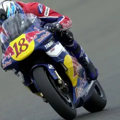 Piloto con casco azul y rojo, traje de carreras Red Bull y moto Yamaha número 18, en plena curva. Jean Michel Bayle en acción.