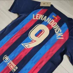 Koszulki meczowe FC Barcelona z nazwiskiem Lewandowskiego i numerem 9. Widoczny też herb UNHCR.