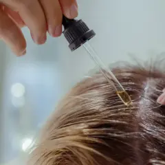 Kropla olejku z witaminą PP aplikowana pipetką na skórę głowy.