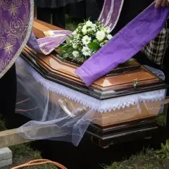 Uroczyste chowanie zmarłego po niedzieli. Trumna z kwiatami, otoczona przez żałobników w strojach liturgicznych, opuszczana do grobu.