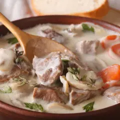 Un réconfortant blanquette de veau facile, servi dans un bol en bois avec une cuillère, garni de persil et de thym.