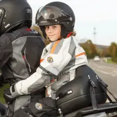 Dziecko w kasku z uśmiechem siedzi z przodu motocykla, gotowe na wspólną podróż. Przewożenie dziecka na motocyklu to przygoda!