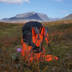 En stor ryggsäck står redo för mat utomhus i fjällterräng. En liggunderlag och en lila kudde syns vid sidan.