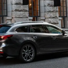 Eleganckie, ciemnoszare kombi Mazda 6, największe kombi na rynku, parkuje przed kamienną fasadą.