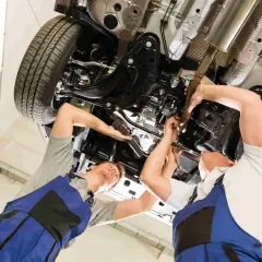 Mechanicy pracują pod samochodem, sprawdzając poduszkę pod silnikiem i inne elementy zawieszenia.