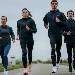 Cztery osoby biegną po drodze, ubrani w sportowe kurtki i legginsy. Wyglądają, jakby właśnie odkryli, kiedy wynaleziono bieganie.