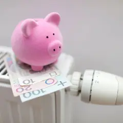 Różowa świnka-skarbonka na grzejniku z polskimi banknotami. Czy to symbol oszczędzania na rachunki, czy bon energetyczny dla każdego?
