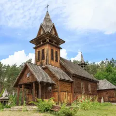 Drewniany kościółek z wieżą i krzyżem, otoczony lasem. Piękny przykład kościołów w Polsce.