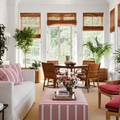 Bright sunroom with white sofa, striped ottoman, rattan chairs, and lush plants. Inspiring sunroom decorating ideas for a fresh, airy feel.
