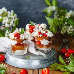 Tre glas med tårta jordgubbar, grädde och färska jordgubbar. Vårligt dekorerat med blommor och gröna blad.