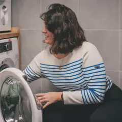 Kobieta w paski wkłada ubrania do pralki. Dowiedz się, jak prać odzież termoaktywną, by służyła latami.