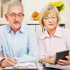 Älteres Paar plant Finanzen, was auf eine **gemeinsame Veranlagung** hindeutet. Mann schreibt, Frau rechnet mit Taschenrechner.