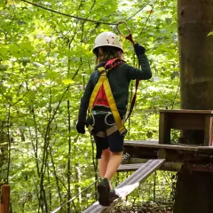 Kind im Hochseilgarten K1 balanciert auf einem schmalen Steg, gesichert durch Klettergurt und Helm.