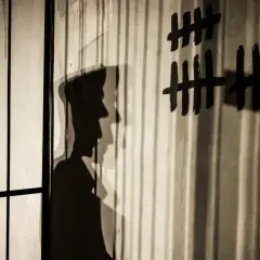 Shadows cast by bars and a figure on a wall with tally marks and letters. This image illustrates how to avoid shadows in indoor photography by using them creatively.