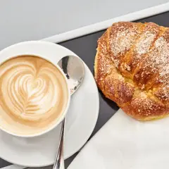 Cappuccino con latte art e brioche americane cosparse di zucchero.