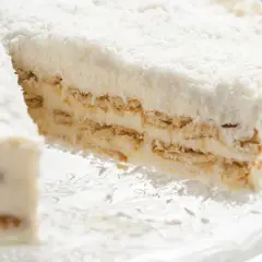 Pyszne rafaello bez pieczenia, warstwowe ciasto z kremem i wiórkami kokosowymi, prezentowane na szklanej paterze.