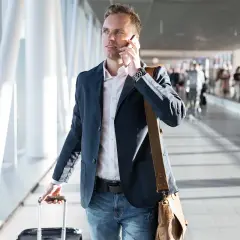 Mężczyzna w marynarce rozmawia przez telefon, ciągnąc walizkę. Może to być podróż służbowa, o której mowa w art. 21 ust. 1 pkt 152 ustawy o podatku dochodowym.