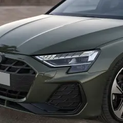 Nowe Audi A3 w zielonym kolorze prezentuje się elegancko. Widoczny fragment maski, grill z logo i reflektor podkreślają jego nowoczesny design.