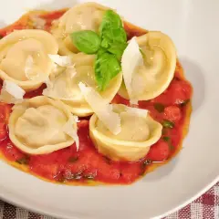 Pyszne ravioli z szynką parmeńską w sosie pomidorowym, posypane parmezanem i udekorowane bazylią.