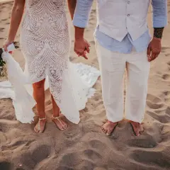 Coppia felice in un matrimonio spiaggia. La sposa con un bouquet, lo sposo con un gilet leggero.