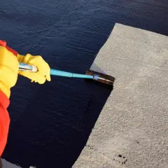 Mit gelben Handschuhen und einem Werkzeug wird das Dach teeren.