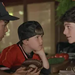Trzej chłopcy w strojach baseballowych, przypominający scenę z filmów dla dzieci z lat 90. Jeden z nich trzyma rękawicę z piłką.