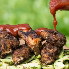 Grillade revbensspjäll toppas med en generös mängd röd bbq sås, serverade på en bädd av gurksallad.