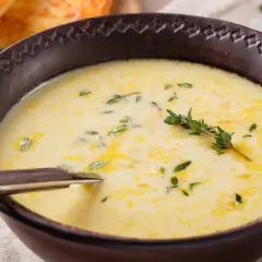 A creamy zupa na rosole, garnished with fresh thyme, served in a rustic bowl with a spoon. In the background, golden-brown toasted bread.
