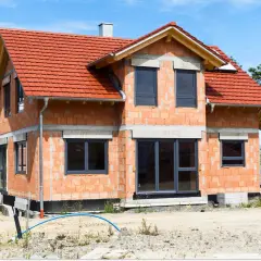 Dom murowany w budowie, z czerwonym dachem i szarymi oknami. Solidna konstrukcja daje pewność, ile lat wytrzyma dom murowany.